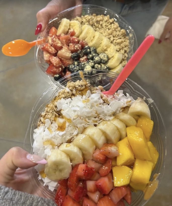 Two açai bowls topped with banana, strawberry, mango, blueberries, coconut flakes and granola.
