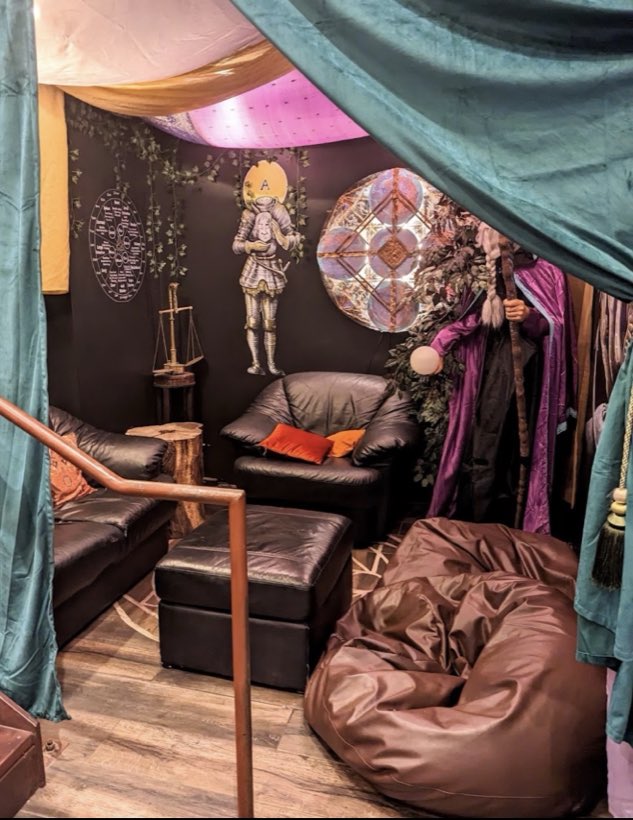 A curtained upstairs alcove with leather seating, alchemy artwork and a velvet cloak.