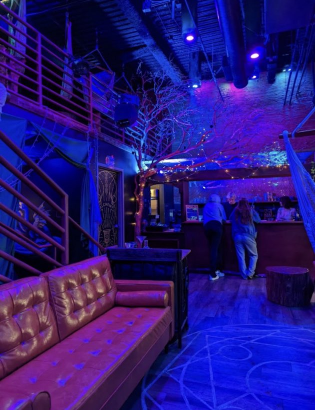 The main room in blue and magenta light — a bare tree strung with fairy lights over the bar.